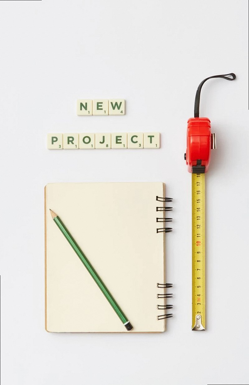 An organized flat lay showcasing a notebook, pencil, tape measure, and scrabble tiles spelling 'New Project'.